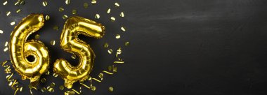 Altmış beş numaralı altın folyo balonu. 65 yazılı doğum günü ya da yıldönümü kartı. Siyah beton arka plan. Yıldönümü kutlaması. Pankart. Boşluğu kopyala