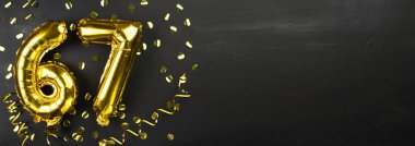 Altmış yedi numaralı altın folyo balonu. 67 yazılı doğum günü ya da yıldönümü kartı. Siyah beton arka plan. Yıldönümü kutlaması. Pankart. Boşluğu kopyala
