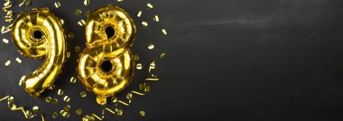98 numaralı altın folyo balonu. 98 yazılı doğum günü ya da yıldönümü kartı. Siyah beton arka plan. Yıldönümü kutlaması. Pankart. Boşluğu kopyala