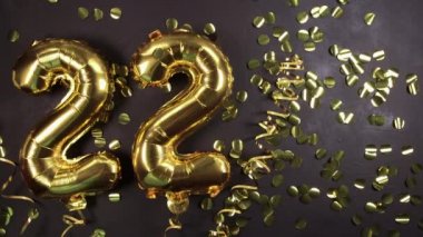 Altın folyo balonu 22 numara. Doğum günü ya da yıldönümü tebrik kartı. Üzerinde 22 yazılıydı. Siyah beton arka plan. Yıldönümü kutlaması.