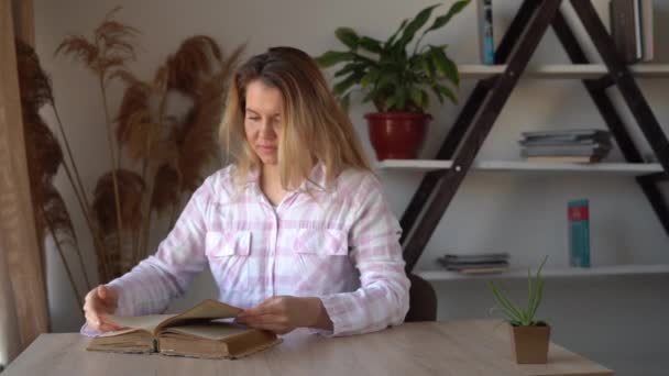 Junge schöne kaukasische Dame, die zu Hause am Tisch sitzt, ein altes Buch liest und die Seiten blättert. Konzept der klugen Frau, die von Büchern lernen kann. — Stockvideo