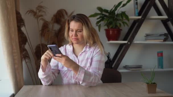 Zblízka radostná dívka čte dobré zprávy po telefonu. Kavkazská dáma sedí doma u stolu a listuje zprávami.. — Stock video