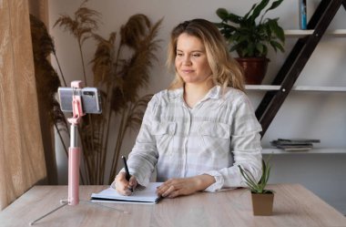 SMS okuyan bir kız akıllı bir telefonla evde bir masada oturuyor ve arka planda bir pencereden gelen sıcak bir ışık var.