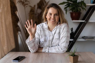 SMS okuyan bir kız akıllı bir telefonla evde bir masada oturuyor ve arka planda bir pencereden gelen sıcak bir ışık var.