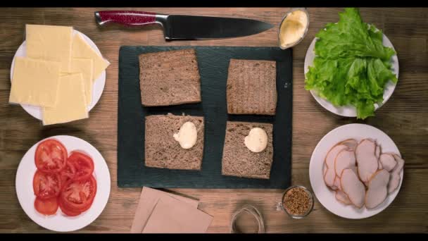 Fermare il movimento, fare panini con carne, formaggio, pomodori ed erbe aromatiche. Pane tostato fresco e ingredienti per una colazione sana. — Video Stock