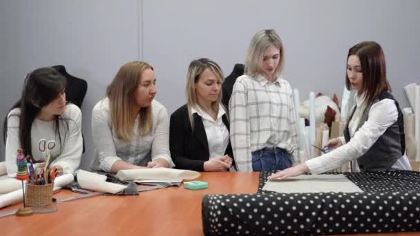 École de créateurs de mode, un maître enseignant dit à un groupe de filles comment couper correctement les tissus. — Video
