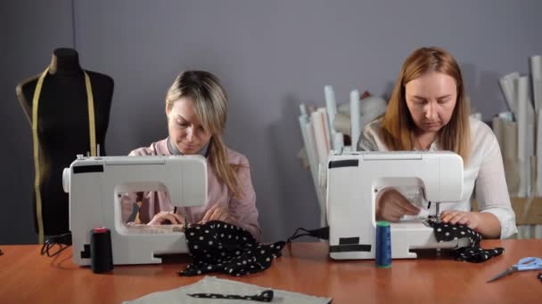 Duas mulheres bonitas cosem com o equipamento profissional em um atelier. Sentam-se à mesa a trabalhar em máquinas de costura. o conceito de produção de coisas. — Vídeo de Stock