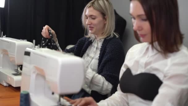 Uma jovem costureira costura tule em uma máquina de costura em uma oficina de costura moderna. Sua colega está trabalhando em uma máquina de costura nas proximidades. — Vídeo de Stock