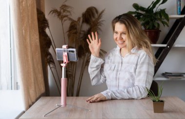 SMS okuyan bir kız akıllı bir telefonla evde bir masada oturuyor ve arka planda bir pencereden gelen sıcak bir ışık var.