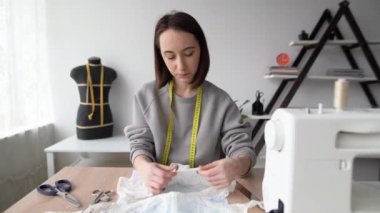 Genç ve güzel bir esmer dikiş makinesinin yanındaki masada oturuyor, kadın külotunu elinde tutuyor ve dikiş kalitesini kontrol ediyor. Kadın tasarımcı iç çamaşırı dikiyor. Küçük işletme.