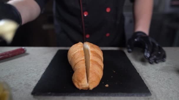 El primer plano de los chefs por las manos ponen la salsa blanca al cruasán con la cuchara. El proceso de hacer un sándwich en la panadería. — Vídeos de Stock