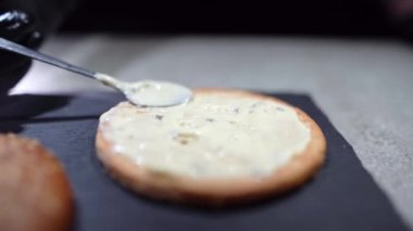 Lezzetli bir hamburger veya çizburger yapma süreci. Şefin eli beyaz sos rulosunun üzerine bir kaşık koyar..