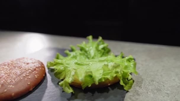 Proces výroby lahodného hamburgeru nebo cheeseburgeru. close-up Chefs hand in gloves puts a fried cutlet on a roll with a salce leaf. — Stock video