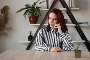 Genç, beyaz, güzel bir iş kadını masada oturmuş akıllı bir telefonla sohbet ediyor. Telefonu kulağına tut..