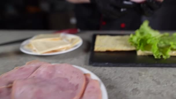 Het proces om focaccia te maken met kalkoenham in de keuken. Chefs handen leggen vlees op een broodje met groene sla. — Stockvideo