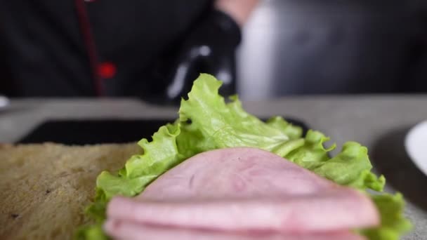 El proceso de fabricación de focaccia con jamón de pavo en la cocina. Chefs manos ponen carne en un sándwich con lechuga verde. — Vídeos de Stock