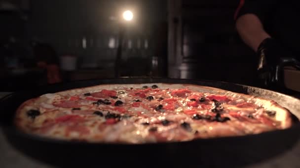 Une grande pizza épicée et délicieuse avec des piments se tient sur la table près du chef. La vapeur monte. Le concept de la cuisine dans une pizzeria ou un fast-food. — Video