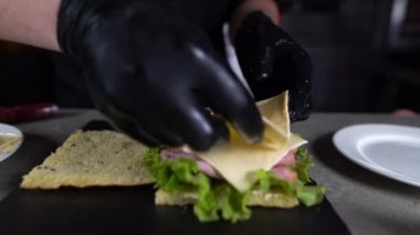 Mutfakta hindi jambonuyla Focaccia yapma süreci. Şefin elleri sandviçin üzerine çedar peyniri koyarken..