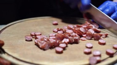Sosisi bıçakla kesmek şefin elinin yakın plan siyah eldiveniyle füme sosisi çabucak keser. Boşluğu kopyala.