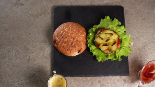 Šéfkuchař připravuje sendvič. Detailní záběr kuchařské ruky připravující vynikající hamburger, který dává sýr čedar na nakládané okurkové plátky a hovězí řízek. plochý ležel. — Stock video