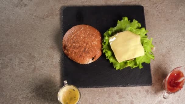 El chef prepara un sándwich. Primer plano de una mano de chefs preparando una deliciosa hamburguesa doble poniendo empanada de carne de res en queso cheddar. plano laico. — Vídeo de stock