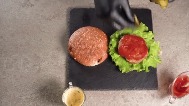 Šéfkuchař připravuje sendvič. Detailní záběr kuchařské ruky, jak připravuje lahodný hamburger a nakrájí kousky nakládané okurky na řízek z hovězího masa. plochý ležel. — Stock video