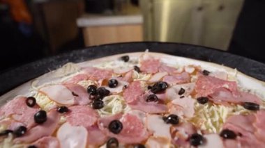 Büyük bir pizza yapma süreci. Şefin elleri siyah eldivenle jambona zeytin koyuyor ve rendelenmiş mozzarella peyniri..