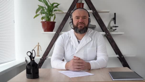 Professional bearded and bald Caucasian male doctor in white medical uniform talking, looking at the camera, doing video chat, conference call or medical seminar, , watching the webcam. — Stock Video