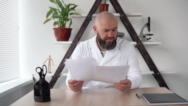 Caucasian male doctor sits and works in a clinic at his workplace, close-up. checking medical documents at the workplace Focused surgeon reading medical uniform analyzing patient diagnosis. — Stock Video