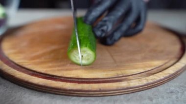 Lastik eldivenli yakın çekim eller tahta kesme tahtasındaki salatalığı kesti. Evde bıçakla sebze doğramak..