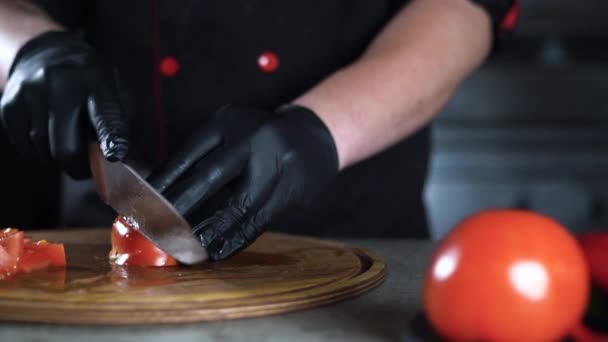 Primer plano de las manos de los chefs en guantes. cortar los tomates rojos con un cuchillo grande en una tabla de cortar. Movimiento de cámara. — Vídeo de stock