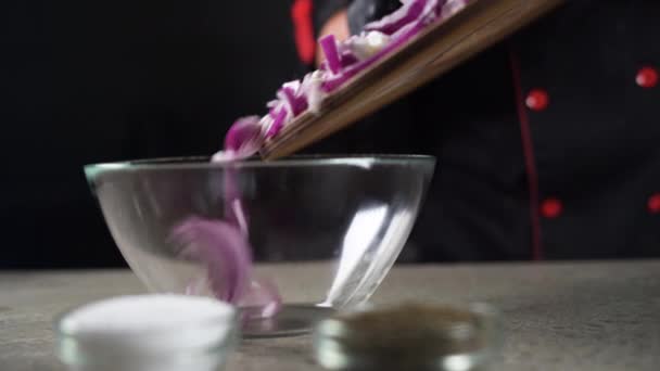Primer plano de las manos de los chefs verter cebolla en rodajas en un recipiente transparente. Ensalada concepto de cocina. — Vídeos de Stock