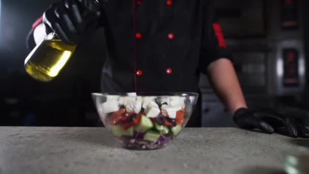 Primer plano de las manos de los chefs vertiendo aceite de oliva en un tazón con ensalada. — Vídeos de Stock