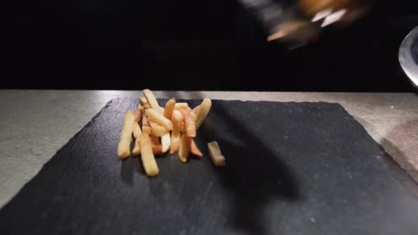 De chef legt gebakken frietjes op een zwart bord. Keukentangen. — Stockvideo