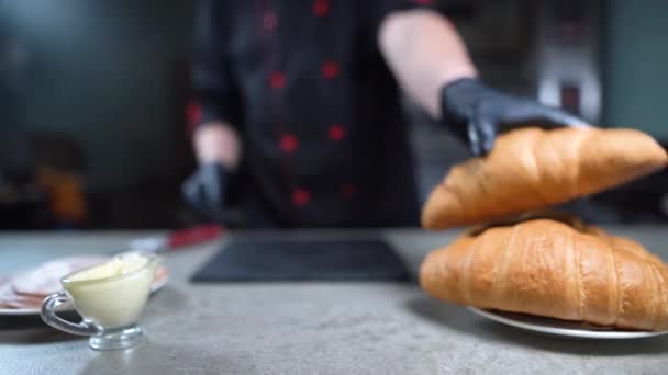 Las primeras manos de un chef con guantes cortan un croissant con un cuchillo afilado. Pasteles apetitosos en una tabla de cortar. Concepto de comida vegetariana saludable. — Vídeos de Stock
