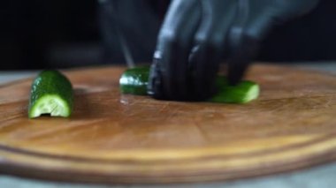 Plastik eldivenli yakın plan eller tahta kesme tahtasındaki salatalığı küp şeklinde kesti. Evde bıçakla sebze doğramak..
