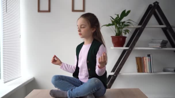 Meditation and relaxation of a little teen sitting on a desk in a lotus position with her legs crossed. Pupil relax rest from online lessons and homework. Healthy girl lunch break. — Stock Video