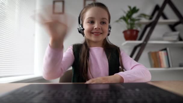 Vrolijke gemotiveerde student 9 's tiener Kaukasische zitten in een koptelefoon op een laptop zwaaien hallo naar de laptop webcam. Online onderwijs videoconferentie gesprek met een buitenlandse leraar. — Stockvideo