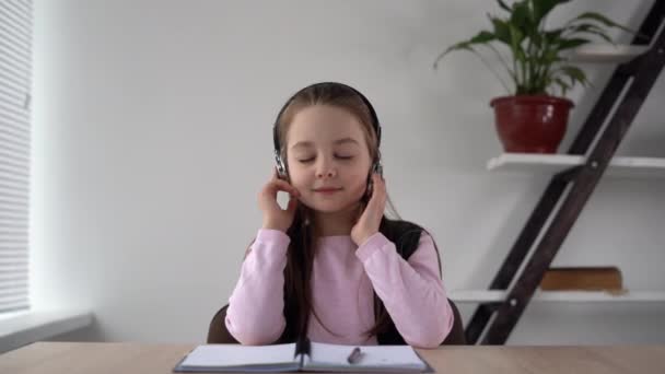 Muzikale pauze van het educatieve proces leerling zitten in draadloze koptelefoon luisteren naar vrolijke muziek langzaam schudden zijn hoofd meezingen. Relaxed schoolmeisje vrouw 8 jaar oud. — Stockvideo