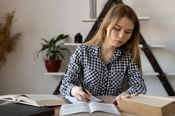 Ένας μαθητής με κίνητρο κάθεται με βιβλία σε ένα γραφείο μελετώντας στο σπίτι. Ένα κορίτσι γράφει για τα μαθηματικά σε ένα σημειωματάριο ή ένας δάσκαλος προετοιμάζεται για μια διάλεξη στο κολέγιο εξ αποστάσεως σε απευθείας σύνδεση. — Φωτογραφία Αρχείου