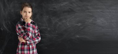 Düşünceli genç bir kız öğrenci ya da tişörtlü bir öğrenci tebeşir tahtasının yanında duruyor. Okul konseptine geri dönelim. Uyarı.