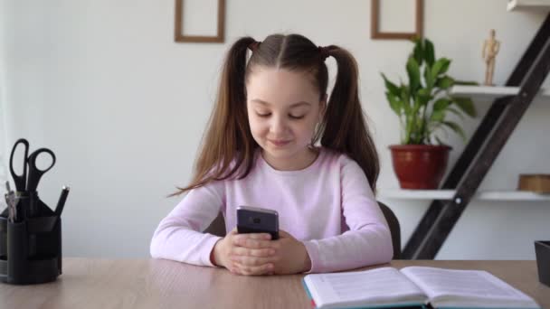 Навязчивая идея школьницы из социальных сетей и интернета с телефоном в руках, сидящей за столом в комнате и изучающей онлайн удаленно с помощью гаджета. — стоковое видео