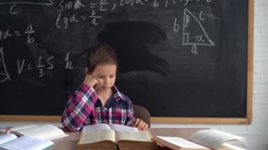 Gömlekli beyaz kız öğrenci formüllü tebeşir tahtasının arka planında oturuyor. Kitap oku. Okula geri dön..