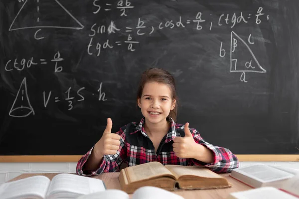 Back to school and happy time. schoolgirl or student studying in the classroom on the background of the blackboard. Caucasian girl looks at the camera and raises her index fingers up. copy space. — Stock Photo, Image