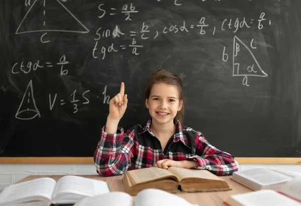 Okula dönelim. Okullu kız, tahtada arka planda ders çalışıyor. Beyaz bir kız kameraya bakar ve işaret parmaklarını kaldırır. Konsept harika bir fikir. Boşluğu kopyala.