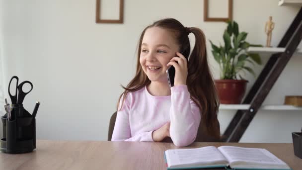 Masasında oturan beyaz bir kız cep telefonuyla konuşuyor, cihaz ve ağ kullanıyor. Genç bir bayan arkadaşıyla cep telefonundan iletişim kuruyor, çalışmalarını ve ödevlerini tartışıyor.. — Stok video