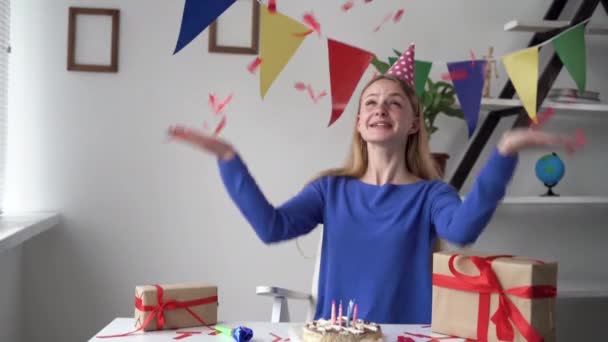 여자는 자기 생일을 집에서 혼자 축하하고 있다. 축제 모자를 머리에 쓰고 있다. 붉은 색종이를 던져 놓고 기뻐 한다. — 비디오