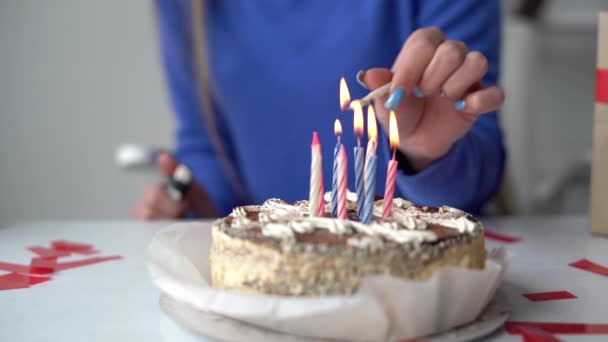 El primer plano de un pastel de cumpleaños está sobre la mesa en casa. Las velas están atascadas en el postre. Las manos femeninas encienden velas en un pastel de cumpleaños. — Vídeos de Stock