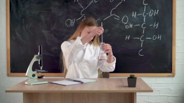 Un chimiste dans un laboratoire chimique effectue des expériences en mélangeant des liquides dans une fiole en verre avec un bâton. Laboratoire de chimie et assistant de laboratoire millénaire à l'école. Concept d'éducation scolaire. — Video