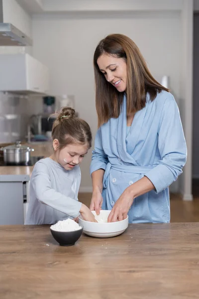 Mutter und Tochter kneten gemeinsam in der Küche Teig in einer Schüssel. Gemeinsam zu Hause kochen. — Stockfoto